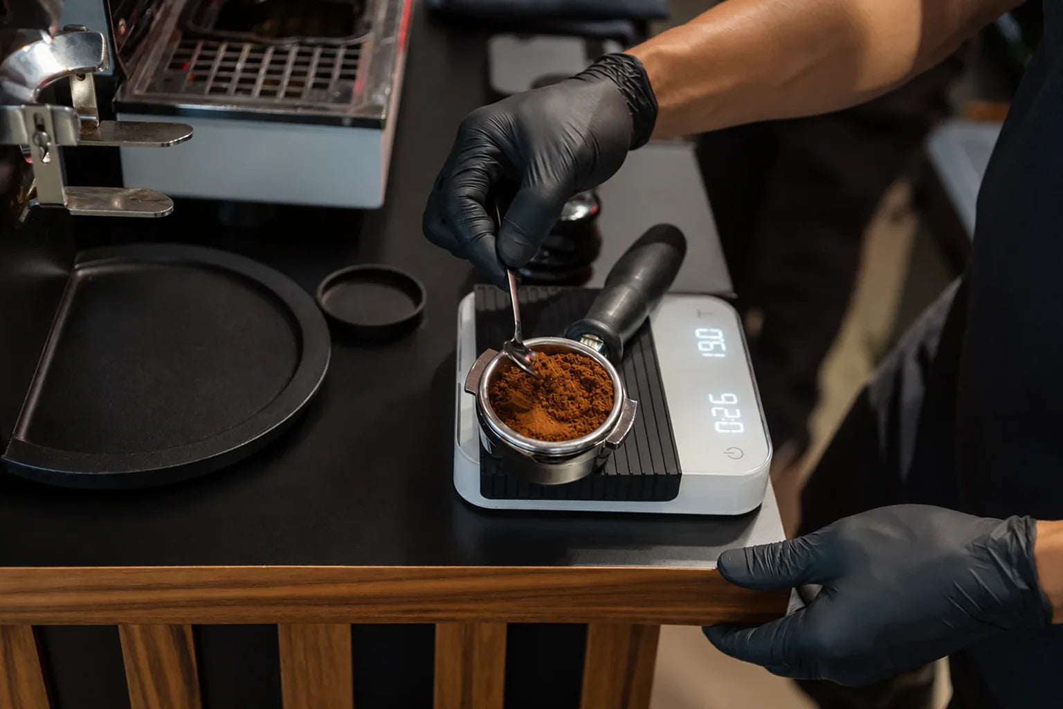 Gloved barista leveling freshly ground coffee in a portafilter